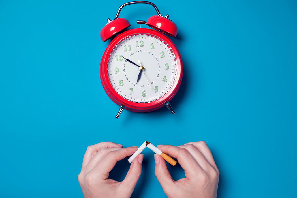 Red alarm clock and hand of woman breaking cigarettes 